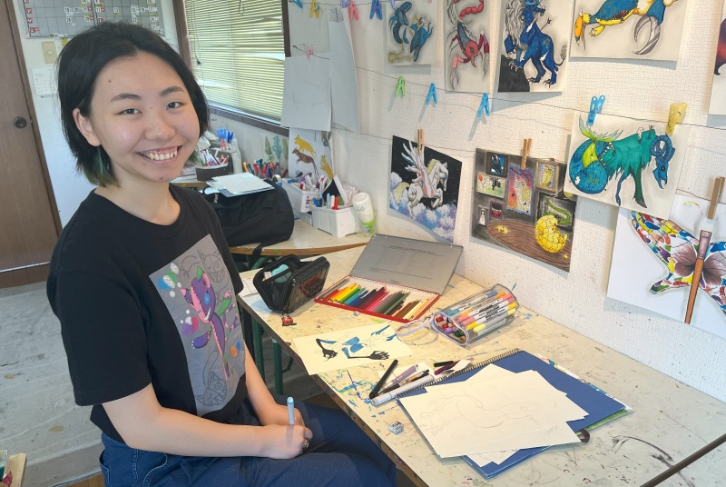 星座のぬいぐるみの絵を前に笑顔を見せる新井さん